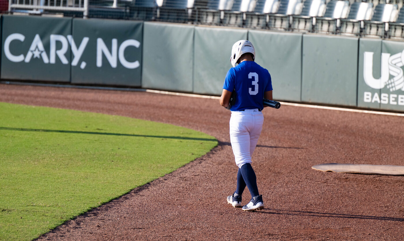 Batter walking the warning track from behind, bat in hand